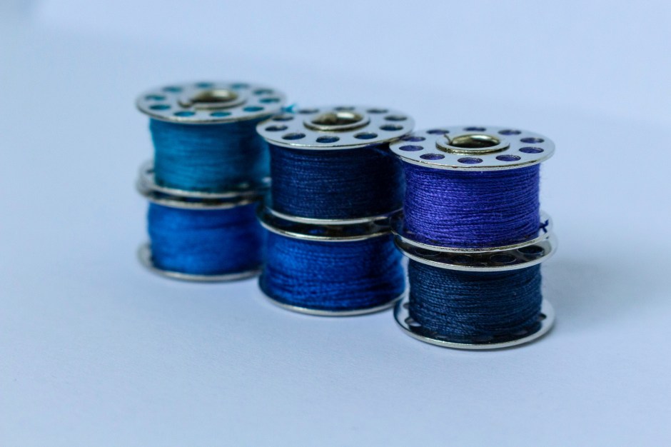 Six sewing bobbins filled with blue and purple thread